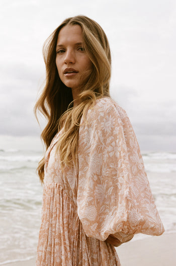 Daughters of India Kyra Maxi Dress in Apricot Blush — side profile at ocean, billowed sleeve and floral print detail