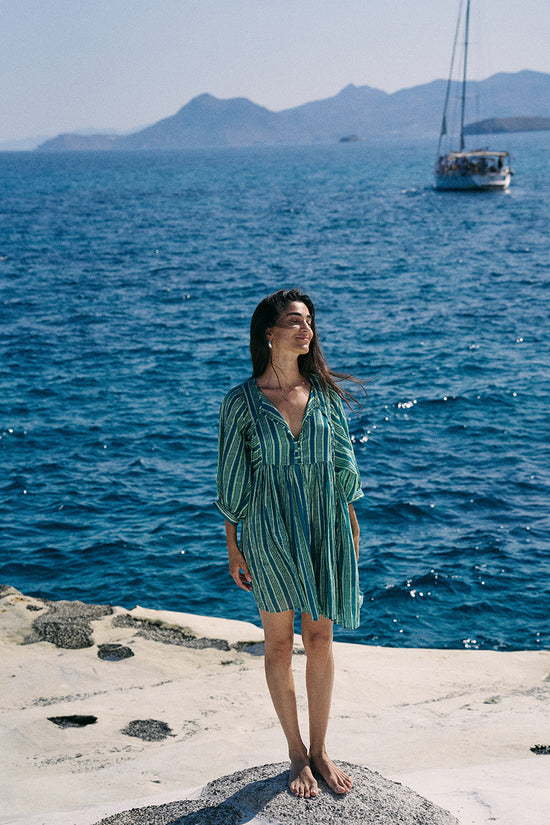 Woman in a green dress standing by the ocean with a boat in the background