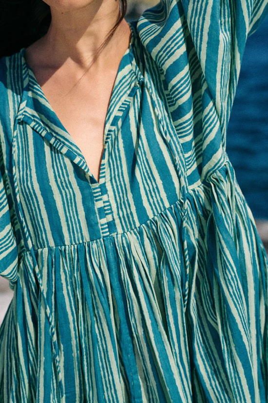 Close-up of a person wearing a blue and white striped dress with a blurred background of the ocean