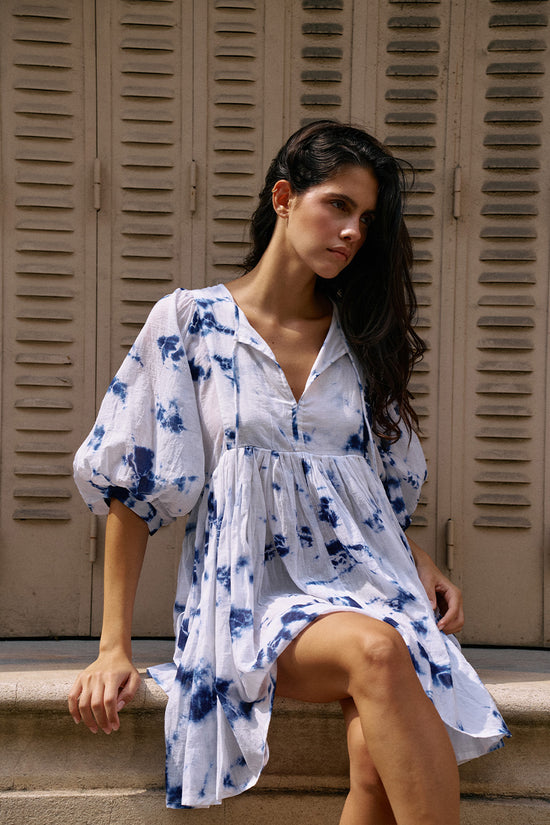 Kyra Mini Dress Deep Sea — close-up front view showing V-neckline tie detail and balloon sleeves, deep sea shibori tie-dye cotton, stone building doorway | Daughters of India
